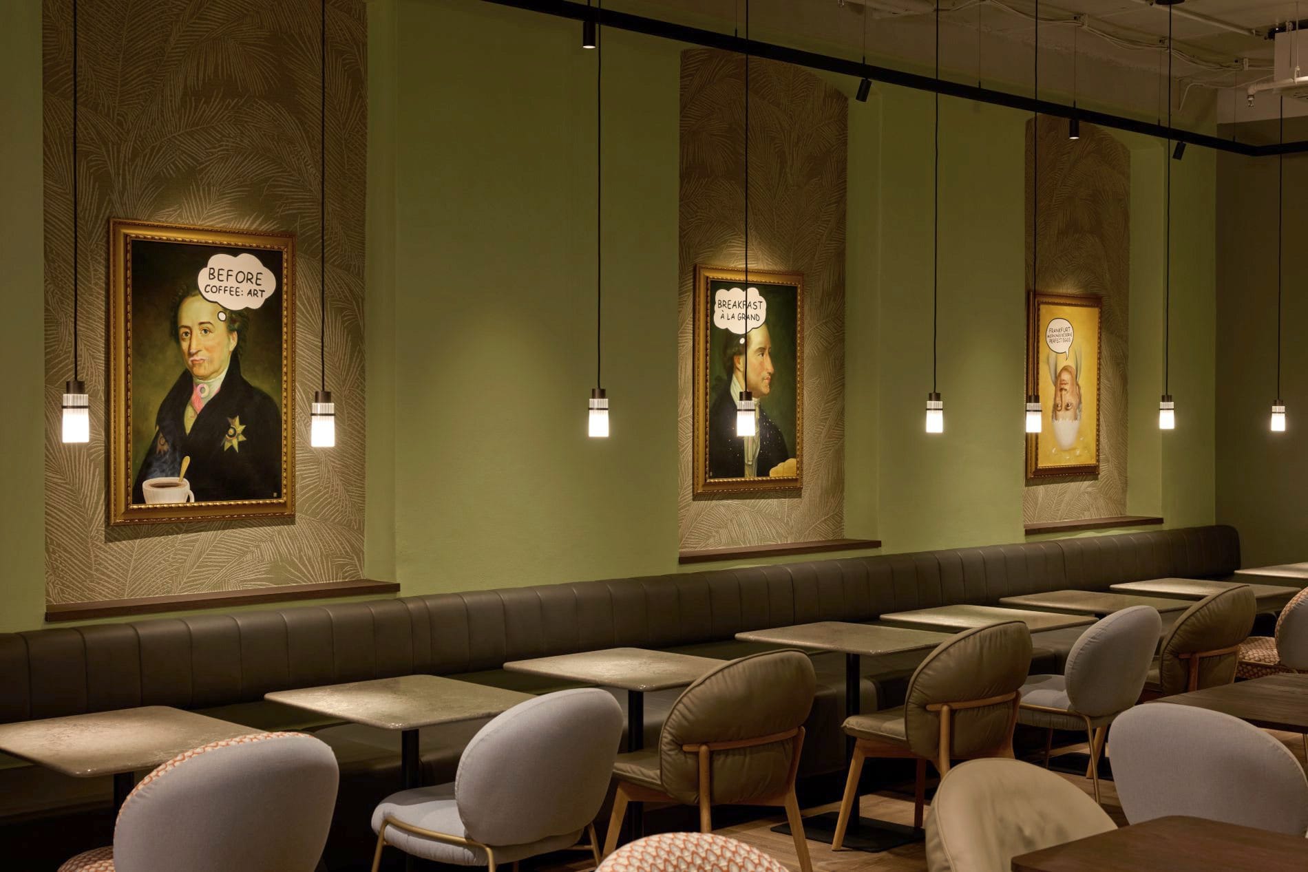 Frühstücksraum mit grünen Wänden, Goethe-Porträts mit Comic-Sprechblasen und gepolsterten Sitzbänken.
