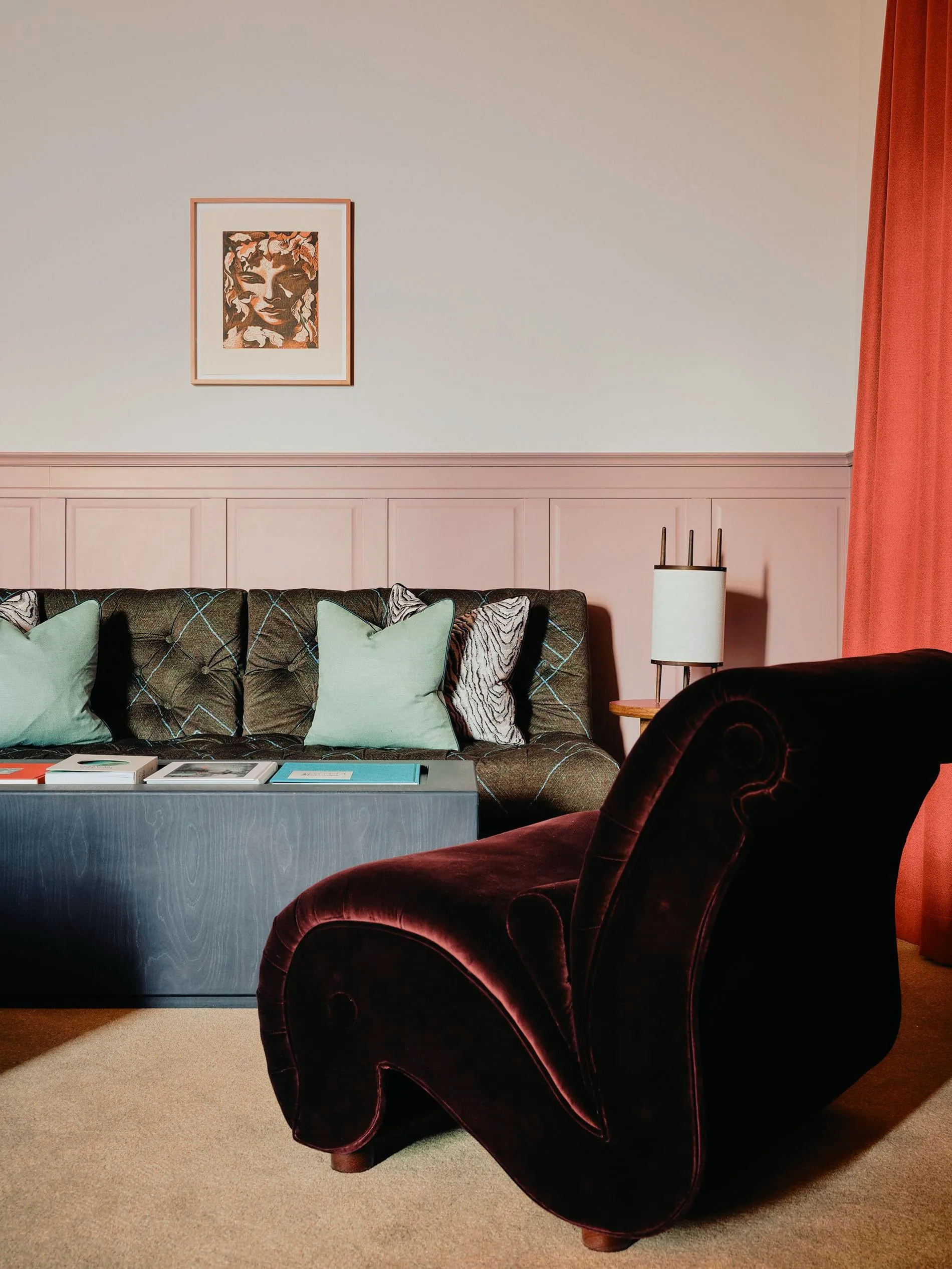 Hingucker: Ein geschwungener Samtsessel in tiefem Bordeaux trifft auf rosa Wandvertäfelung und ein Werk aus der „Wanderers"-Sammlung von Kurator Thom Oosterhof.