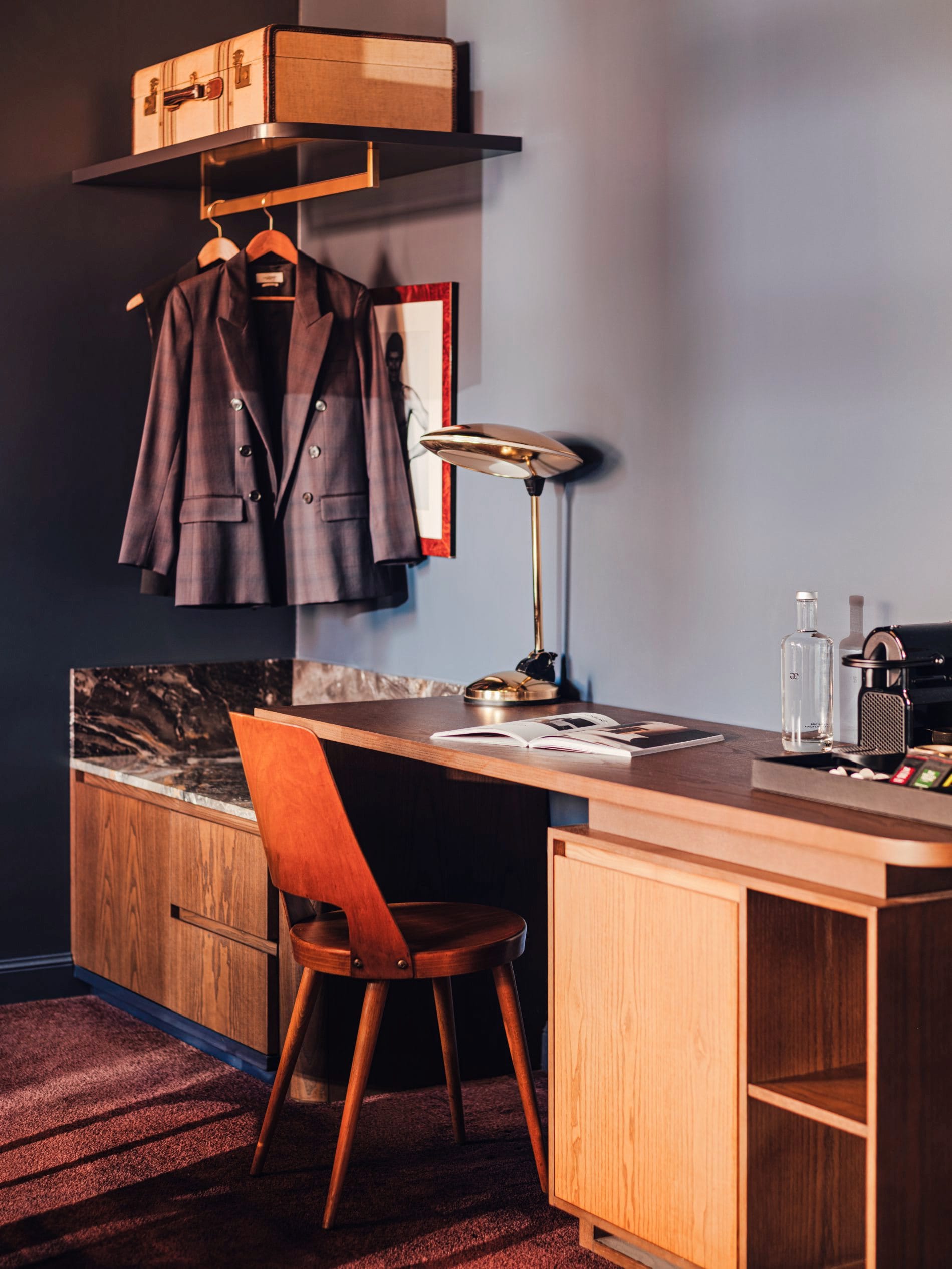 Ein Vintage-inspirierter Arbeitsbereich einem der Zimmer mit Mid-Century-Stuhl, Messing-Schreibtischlampe und offenem Garderobenkonzept.