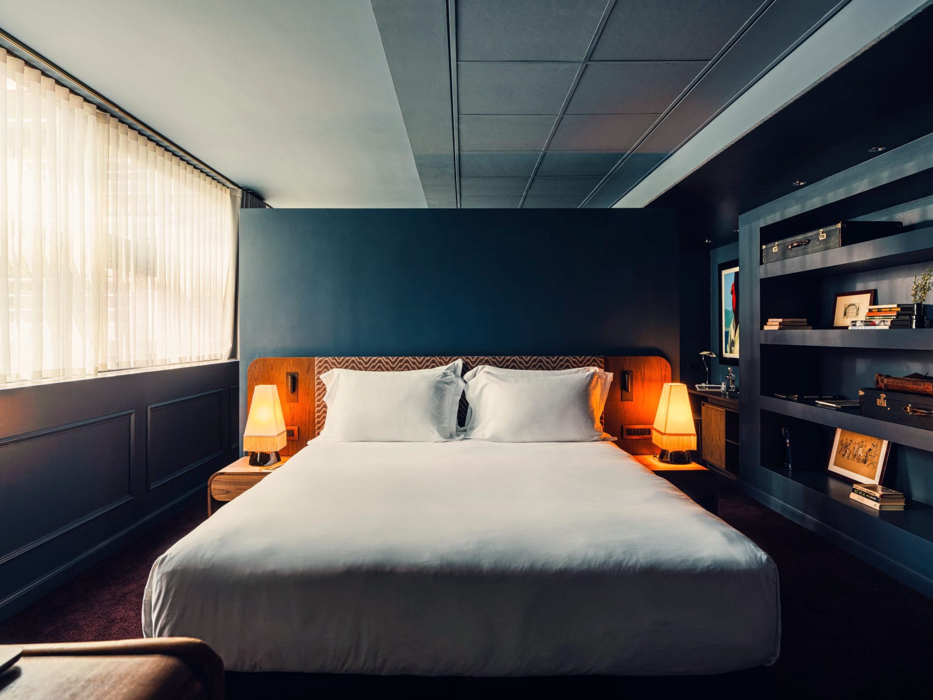 In der Townhouse Suite dominieren tiefes Petrolblau, Holzakzente und ein offenes Bücherregal mit Vintage-Accessoires.