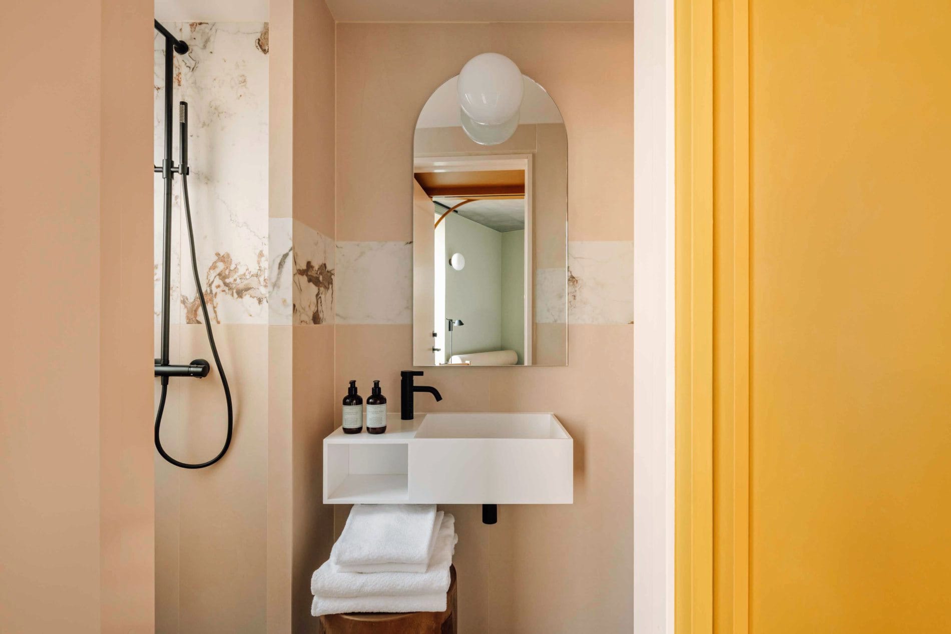 Rosafarbene Wandfliesen setzen warme Akzente im Badezimmer. Schwarze Armaturen und ein gewölbter Spiegel mit Kugelleuchte unterstreichen den skandinavisch-modernen Stil.