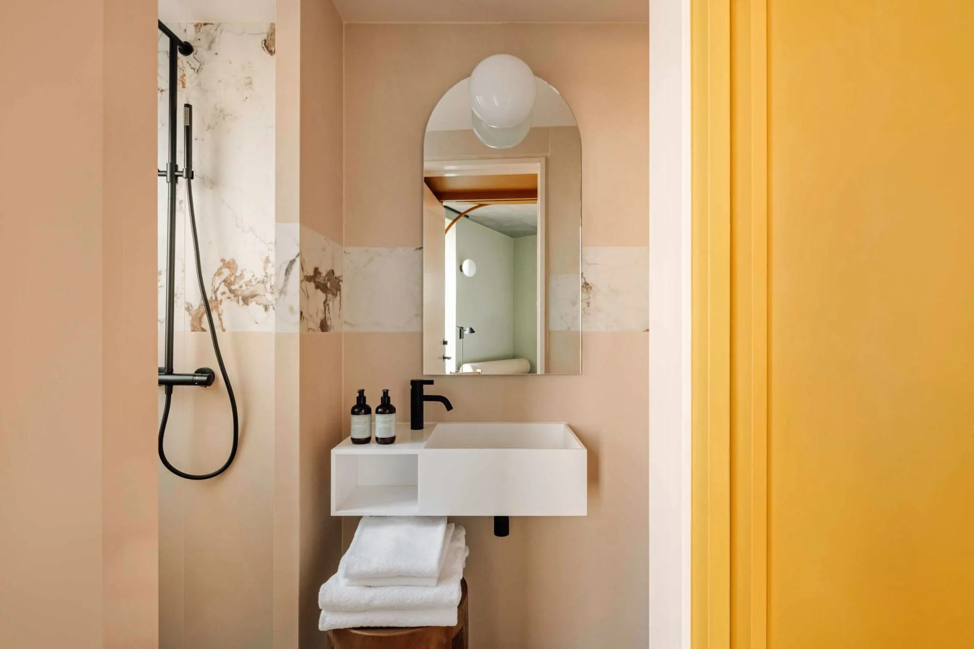 Rosafarbene Wandfliesen setzen warme Akzente im Badezimmer. Schwarze Armaturen und ein gewölbter Spiegel mit Kugelleuchte unterstreichen den skandinavisch-modernen Stil.