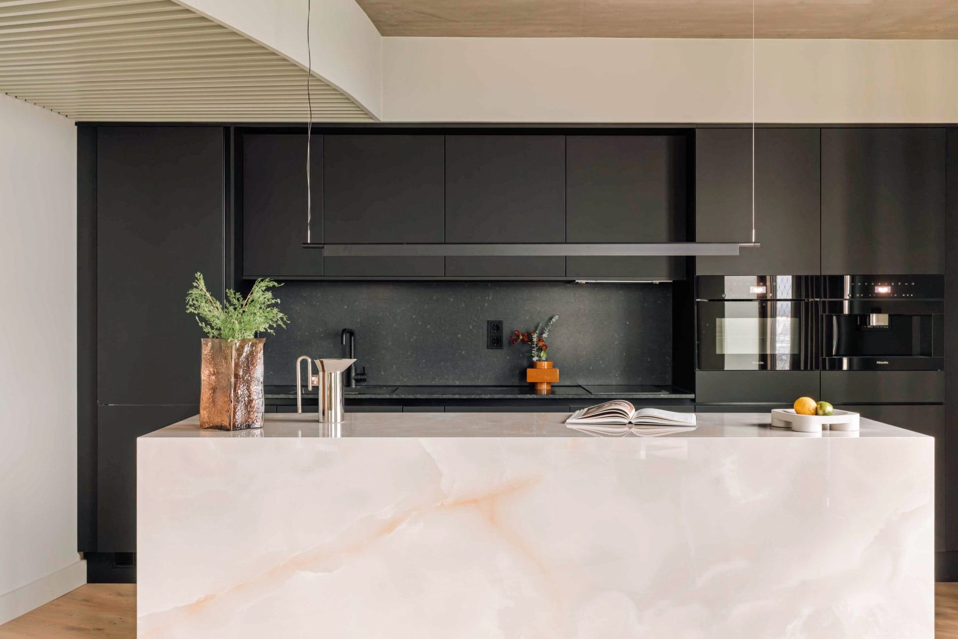 Die Penthouse-Küche verbindet eine großzügige Kochinsel aus hellem Onyx-Marmor mit schwarzen Miele-Einbaugeräten.