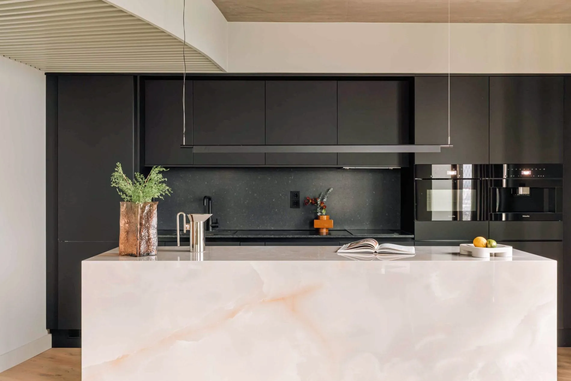 Die Penthouse-Küche verbindet eine großzügige Kochinsel aus hellem Onyx-Marmor mit schwarzen Miele-Einbaugeräten.