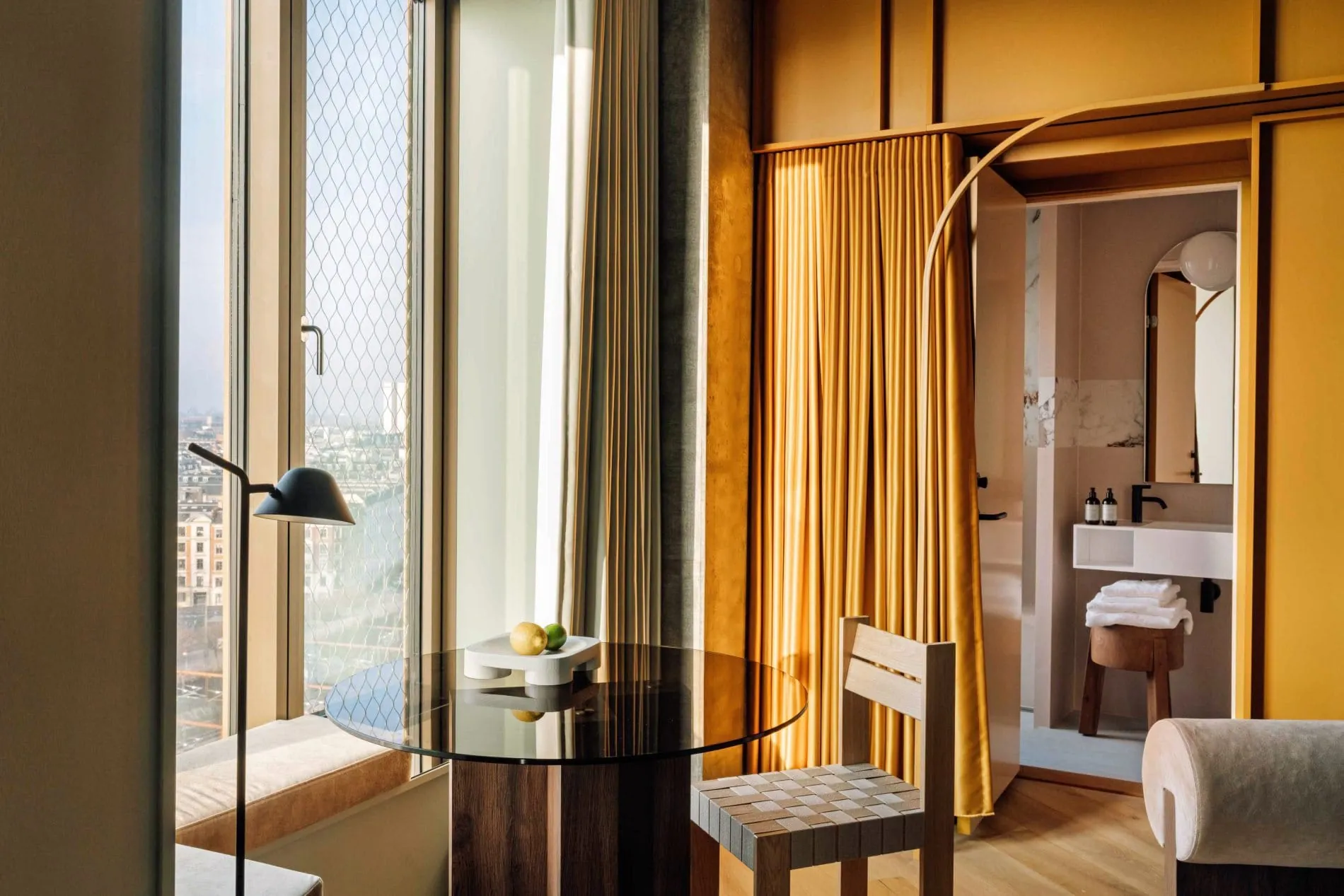 Ein runder Glastisch mit geflochtenem Holzstuhl bildet den Arbeits- und Essbereich am Fenster. Durch die raumhohen Fenster eröffnet sich der Blick über die Kopenhagener Stadtlandschaft.