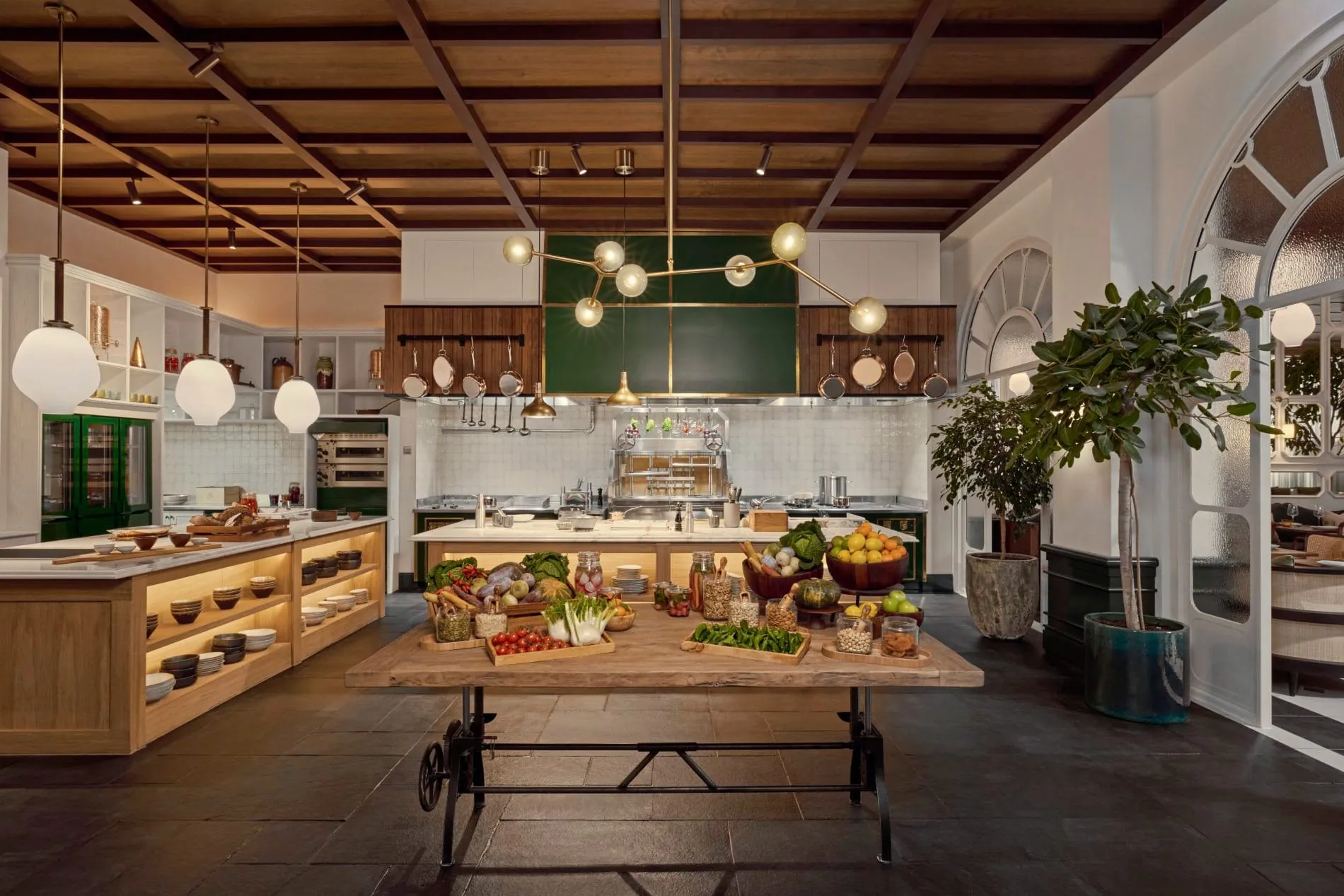 Frisches Gemüse und Obst auf einem mobilen Holztisch stehen im Zentrum der offenen Küche.