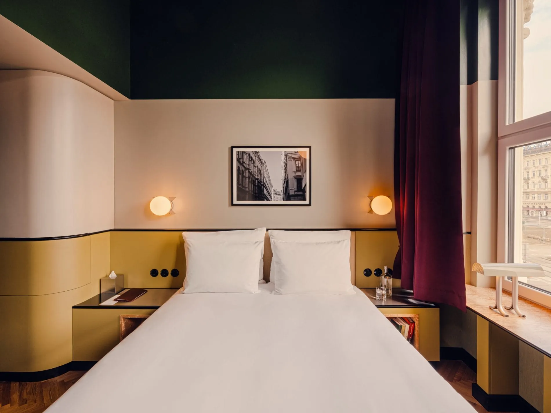 Dunkelgrüne Decken, senfgelbe Wandpaneele und ein Schwarz-Weiß-Foto über dem Bett prägen die Zimmergestaltung. Die Grundrisse folgen nicht dem Standardraster, sondern der Geometrie des historischen Gebäudes – jede Kategorie hat ihren eigenen Charakter.