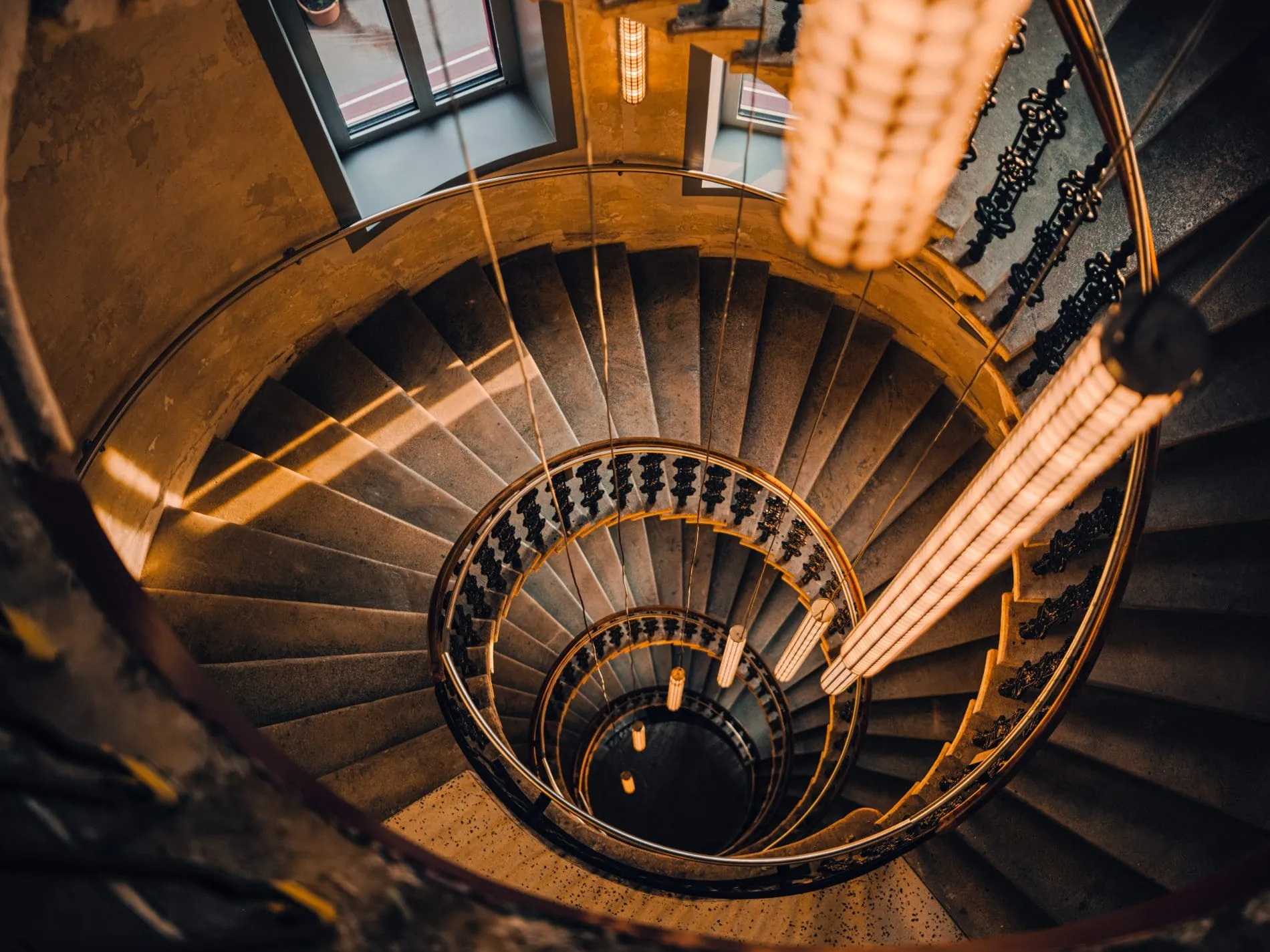 Die spiralförmige Wendeltreppe mit schmiedeeisernem Geländer gehört zur historischen Bausubstanz des Gebäudes. Beleuchtete Gitterleuchten begleiten den Treppenverlauf über mehrere Stockwerke hinweg.