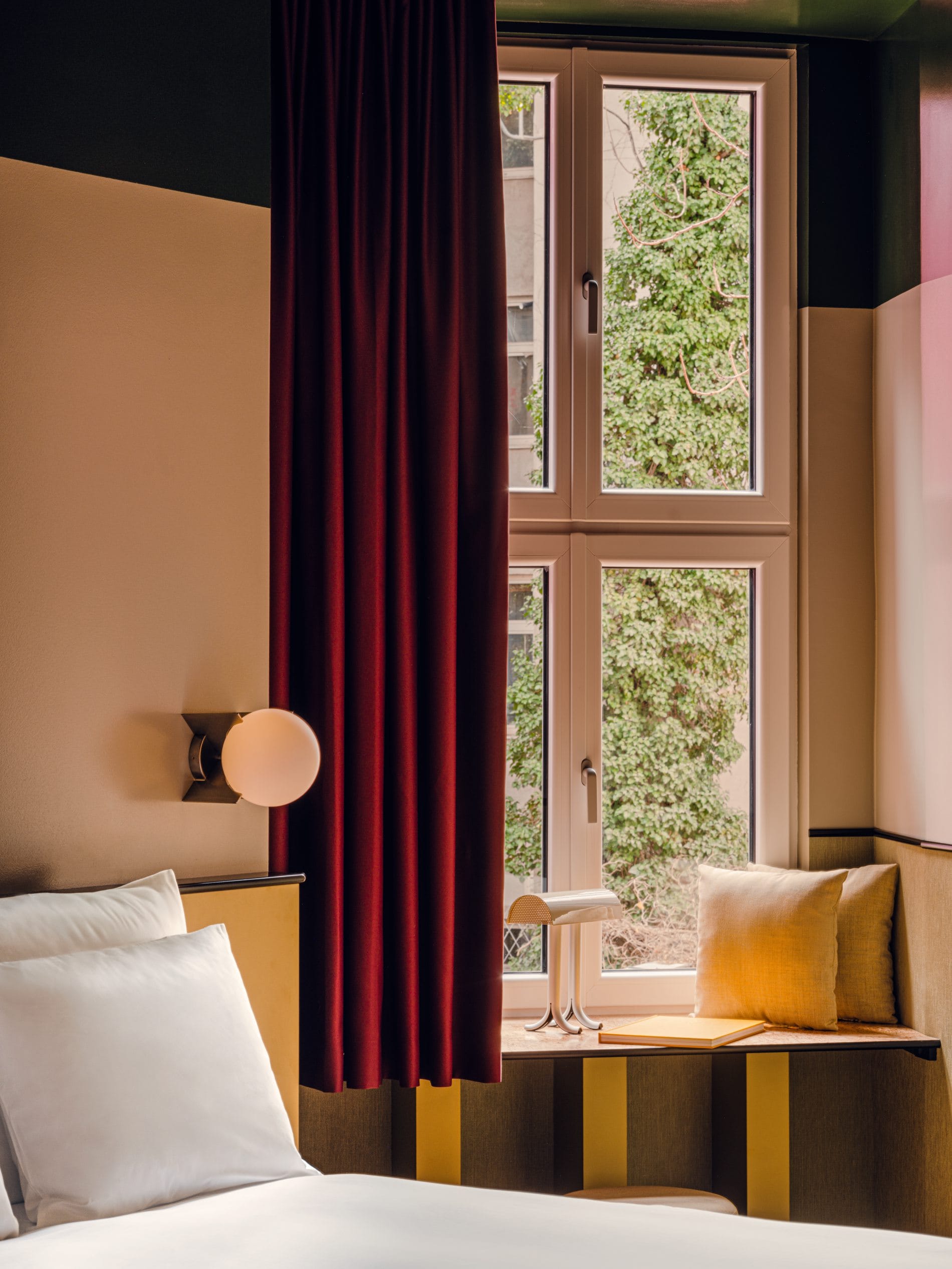Bordeauxrote Samtvorhänge, senfgelbe Polster und eine kugelförmige Wandleuchte bestimmen das Farbspiel in den Zimmern.