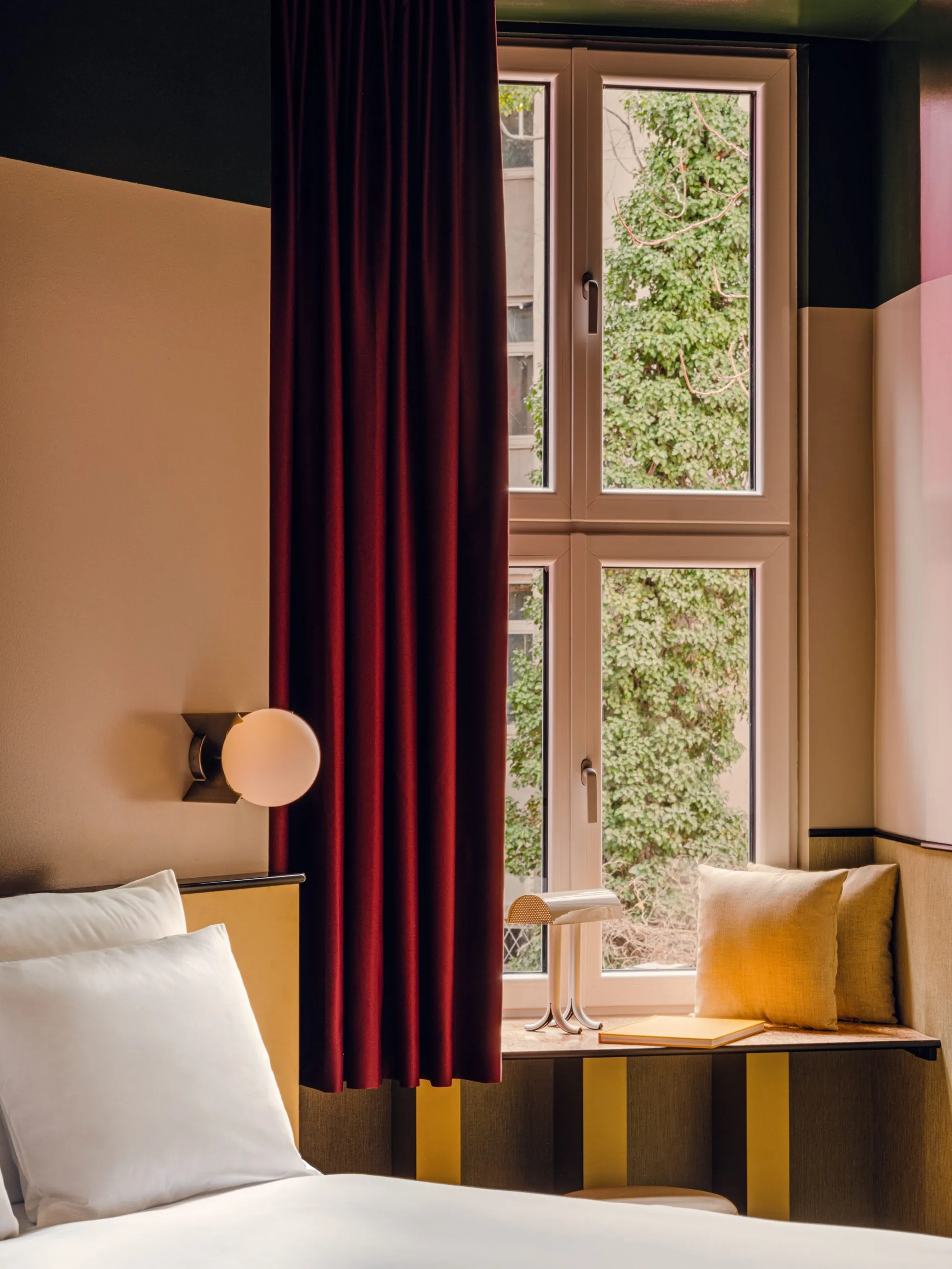 Bordeauxrote Samtvorhänge, senfgelbe Polster und eine kugelförmige Wandleuchte bestimmen das Farbspiel in den Zimmern.