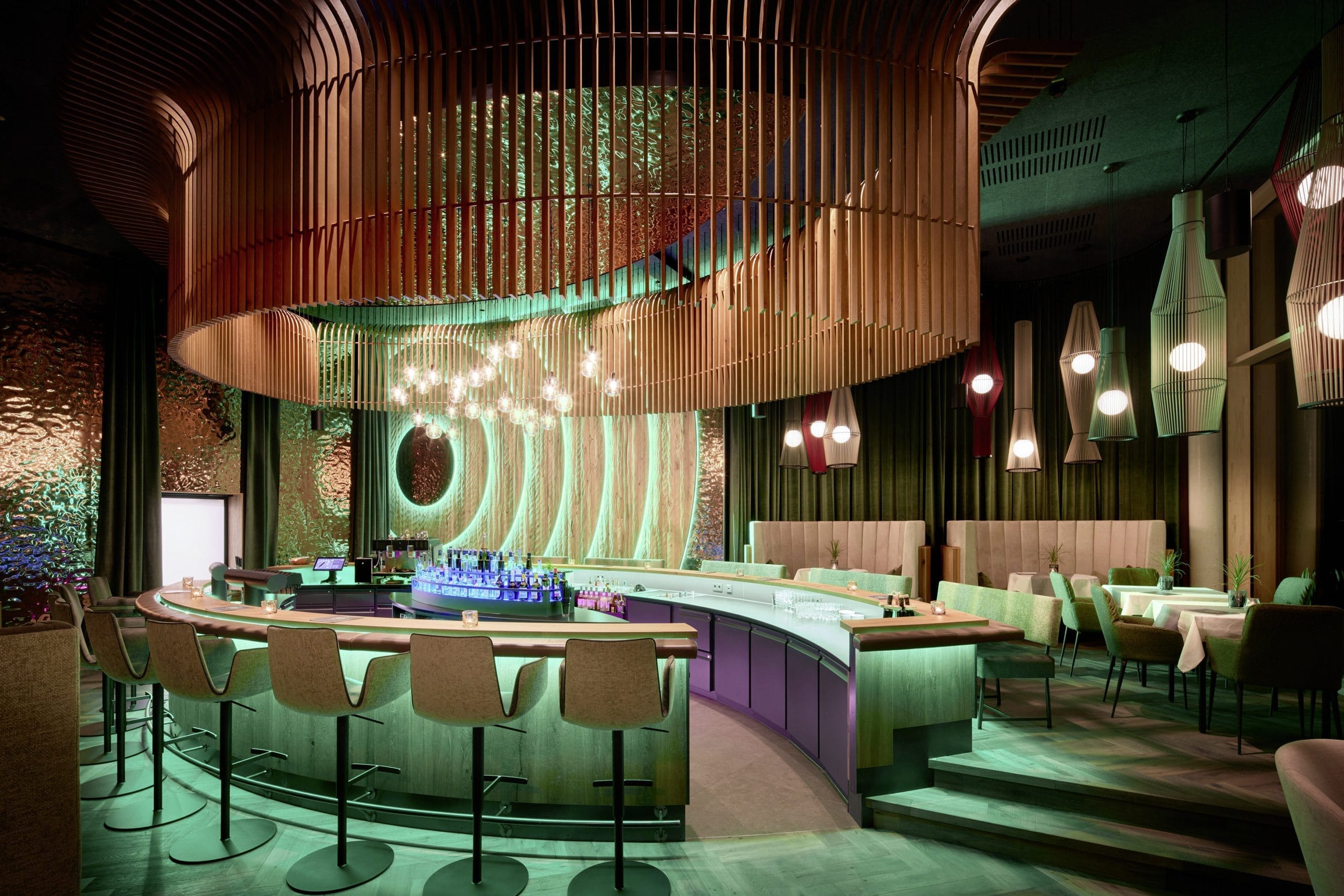 Die Hotelbar „I-Dipferl“ im Wellnesshotel Riedlberg in Drachselried zeichnet sich durch eine Raumhöhe von über fünf Metern und großzügige Glasflächen aus. Das Zusammenspiel von Licht, Akustik und Architektur – unter anderem durch den Einsatz von RGB-Beleuchtung und einem hochwertigen Soundsystem – soll für eine entspannte Atmosphäre sorgen.