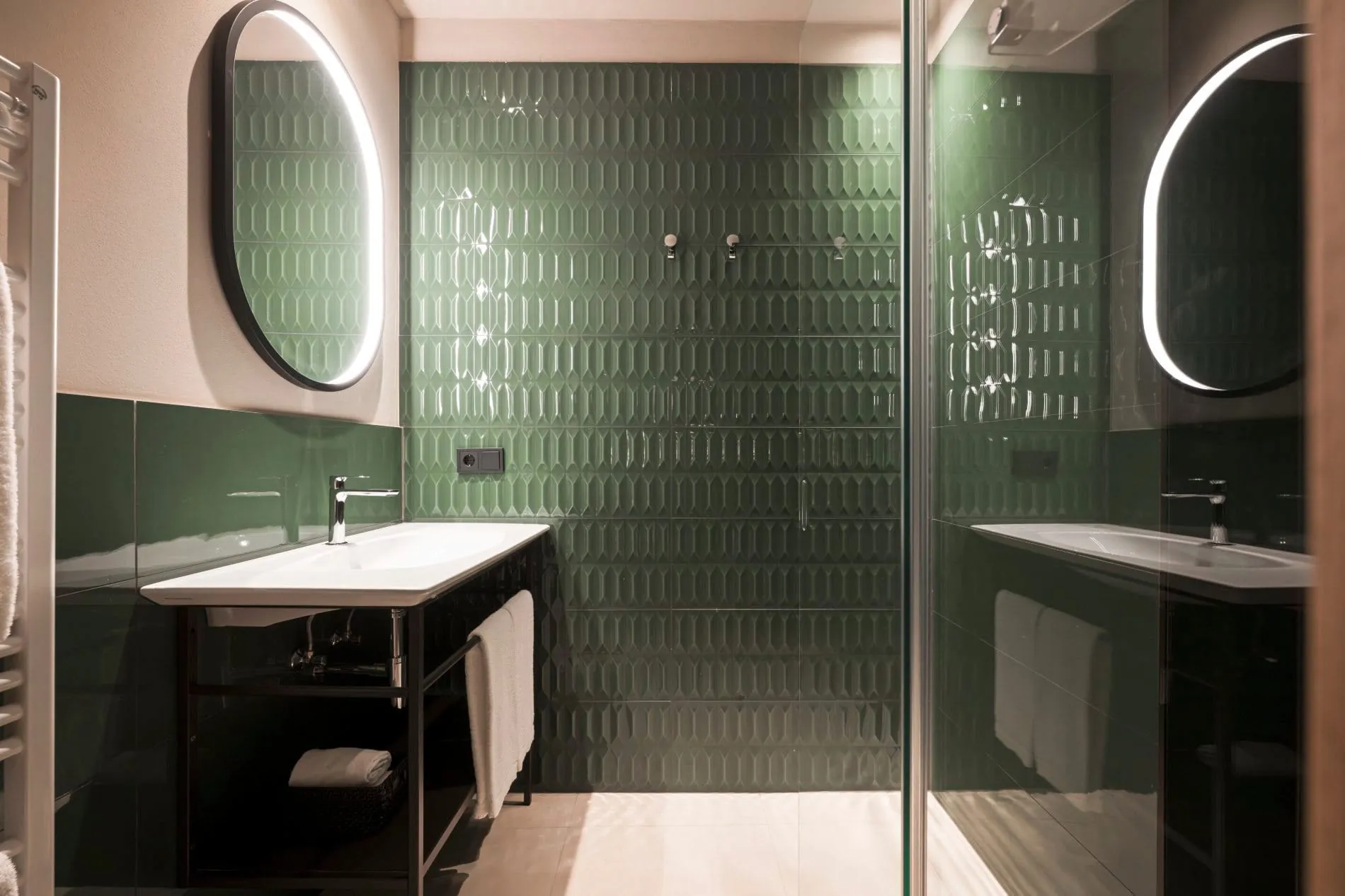 Strukturierte Smaragdfliesen und ovale LED-Spiegel verleihen dem Badezimmer der Suite Panorama einen Retro-Charme, der das gestalterische Konzept des Hauses zwischen Tradition und Moderne widerspiegelt.