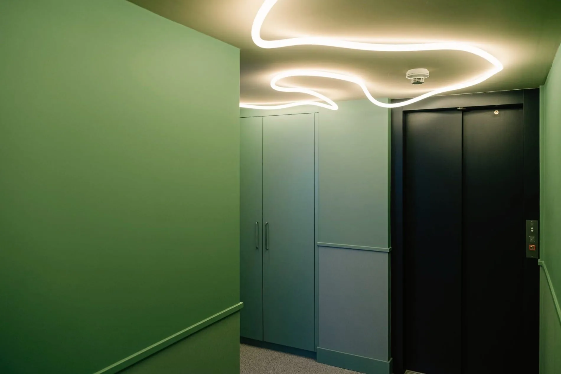 Auch Flure werden durch grüne Wandflächen und organisch geformte Leuchtbänder von Artemide als eigenständige Designräume inszeniert.
