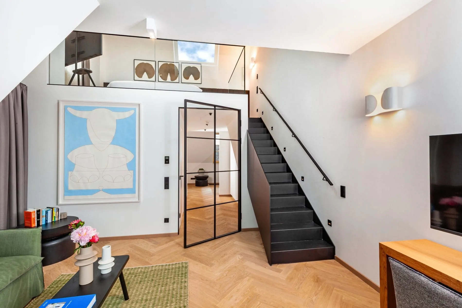 Der großzügige Wohnbereich der Duplex-Suite zeichnet sich durch ein offenes Design über zwei Etagen aus, die durch eine Treppe verbunden sind. Große Kunstwerke setzen farbliche Akzente im Raum.