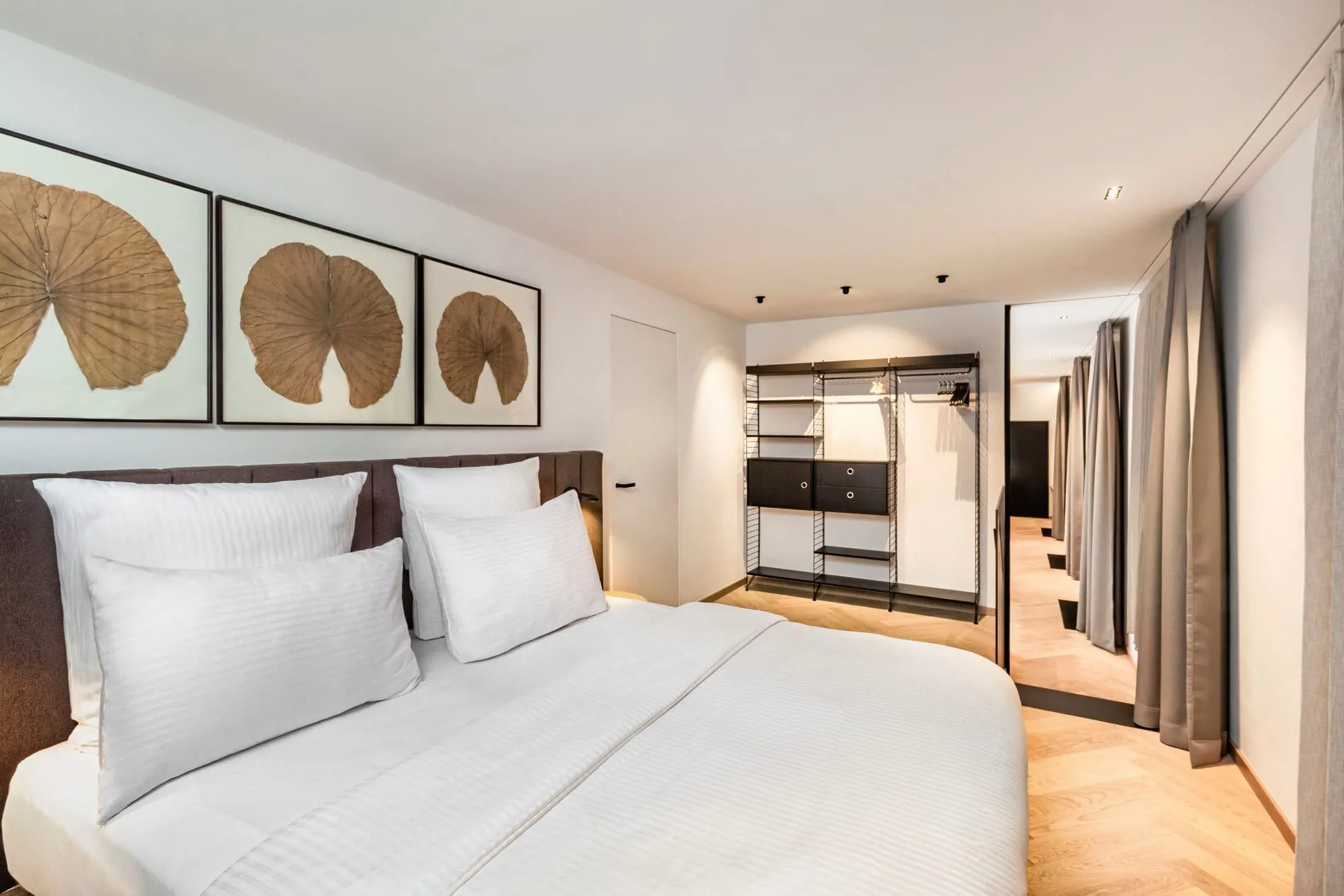 Im Schlafzimmer der Schaezler-Suite schaffen ein harmonisches Farbkonzept und stilvolle botanische Kunstwerke über dem Doppelbett eine ruhige Atmosphäre. Ein offenes Regalsystem ergänzt die Einrichtung und bietet eleganten Stauraum.