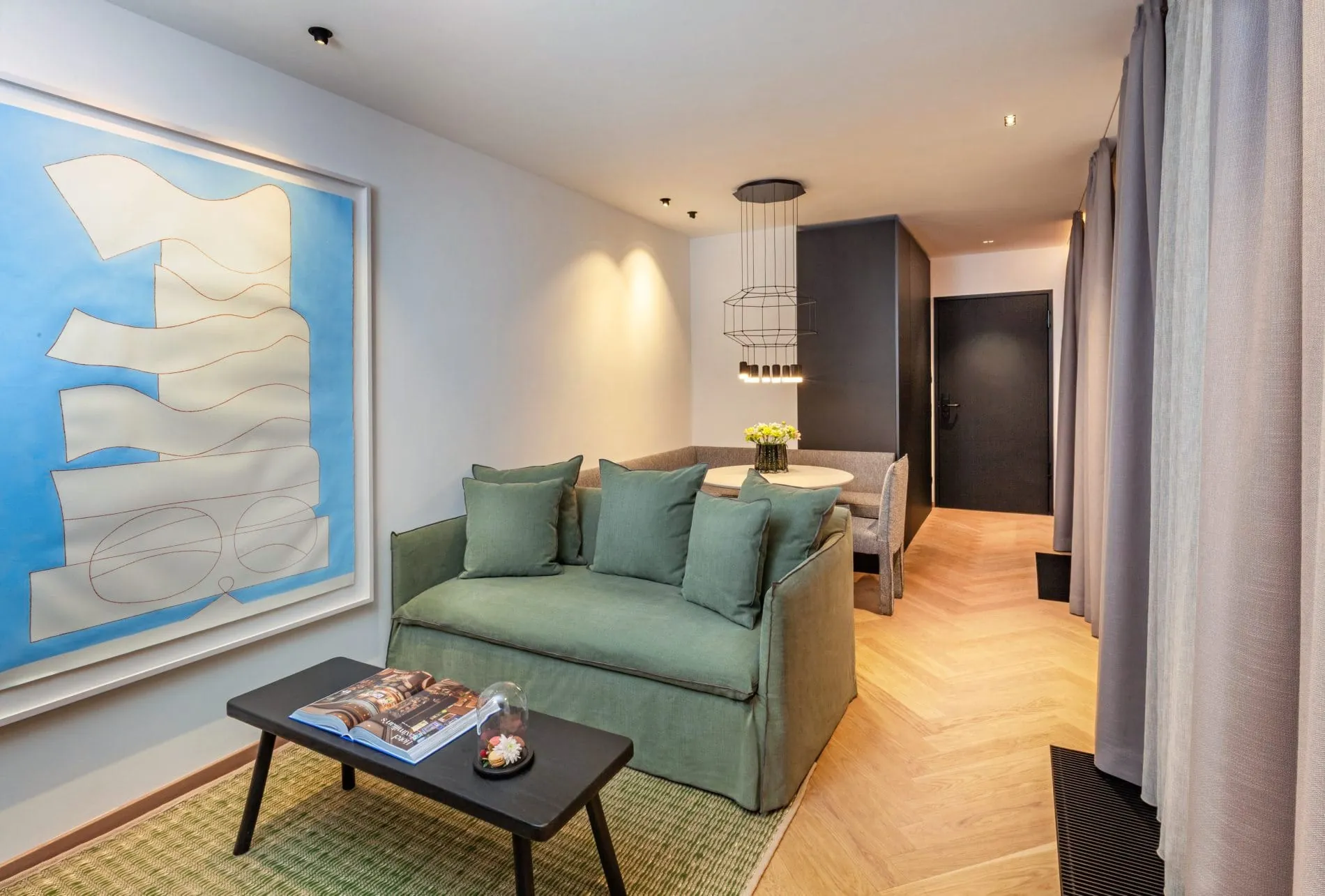 Im Wohnbereich der Schaezler-Suite lädt ein grünes Sofa zum Verweilen ein, während im Hintergrund eine Sitzecke für gemeinsame Mahlzeiten bereitsteht.
