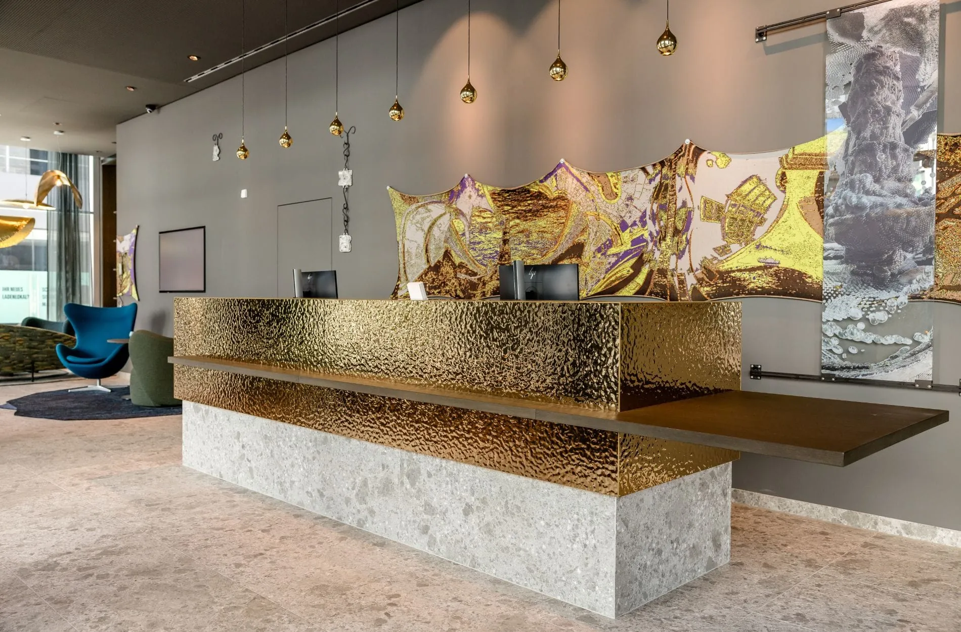 Wasserinspirierte Strukturen sowie Akzente in Goldtönen prägen den Empfangsbereich des Motel One Koblenz.
