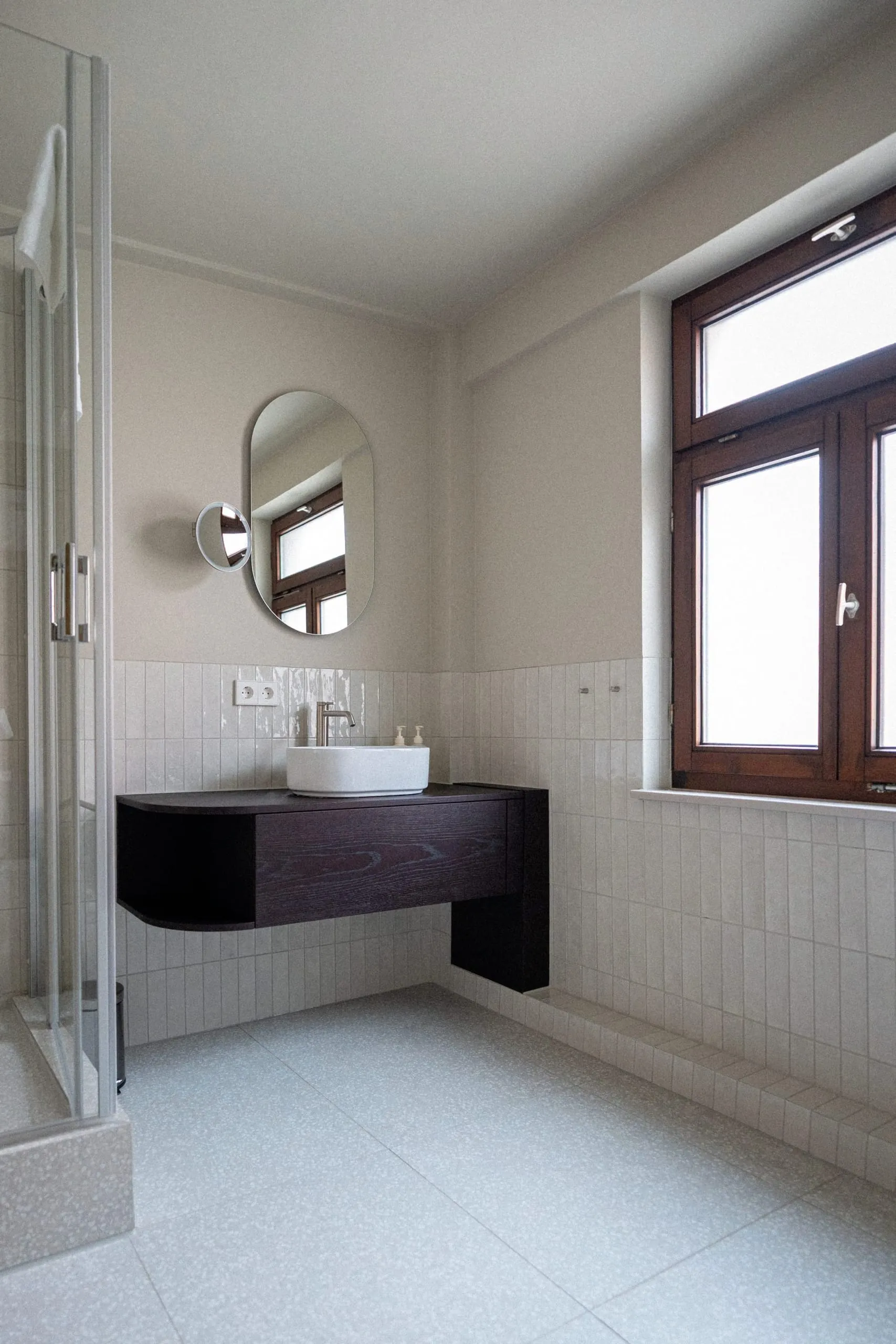 Die großzügigeren Badezimmer zeichnen sich durch ein klares Design aus. Ein dunkler, schwebender Waschtisch kontrastiert mit den hellen Fliesen.