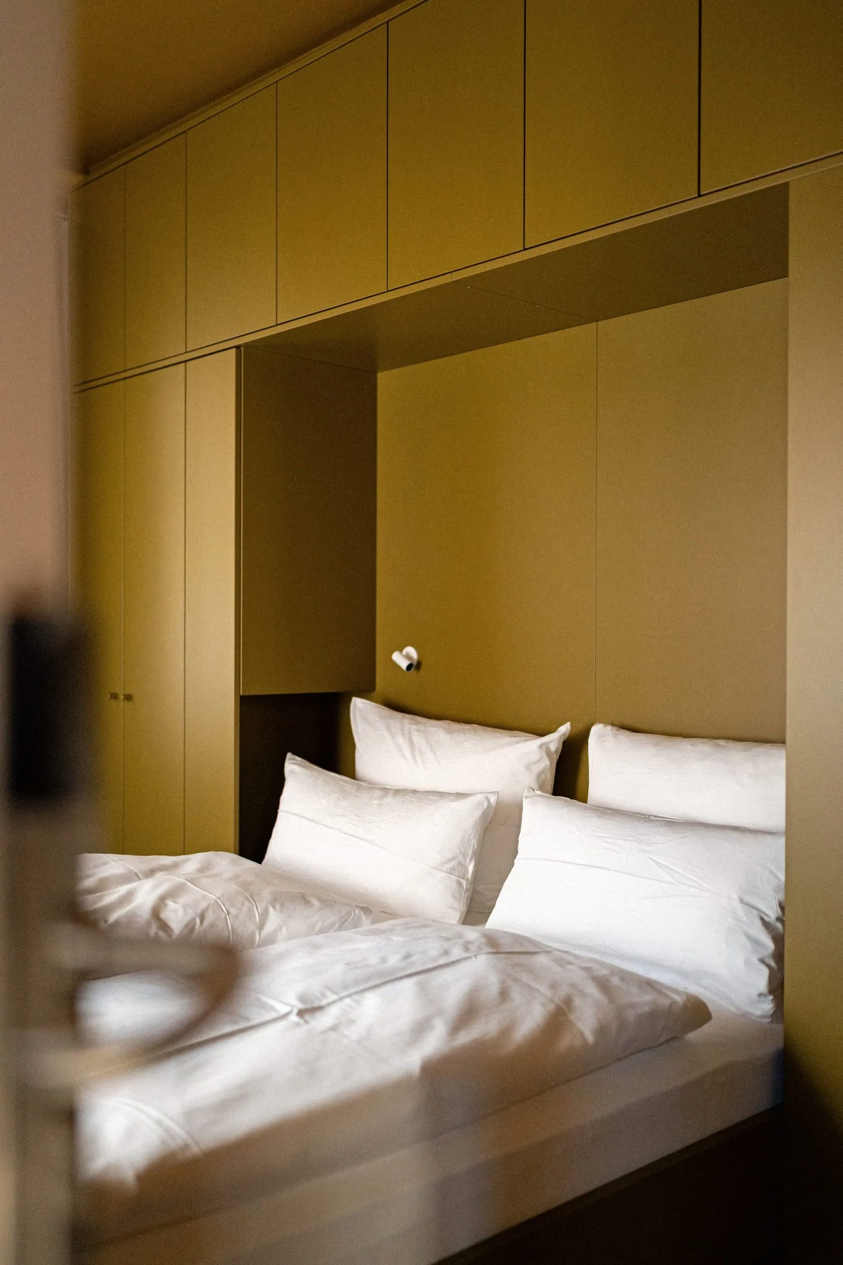 Die Farbwelt Lush Olive verleiht diesem Gästezimmer eine beruhigende, erdige Note. Maßgeschneiderte Einbauschränke umrahmen das Bett.