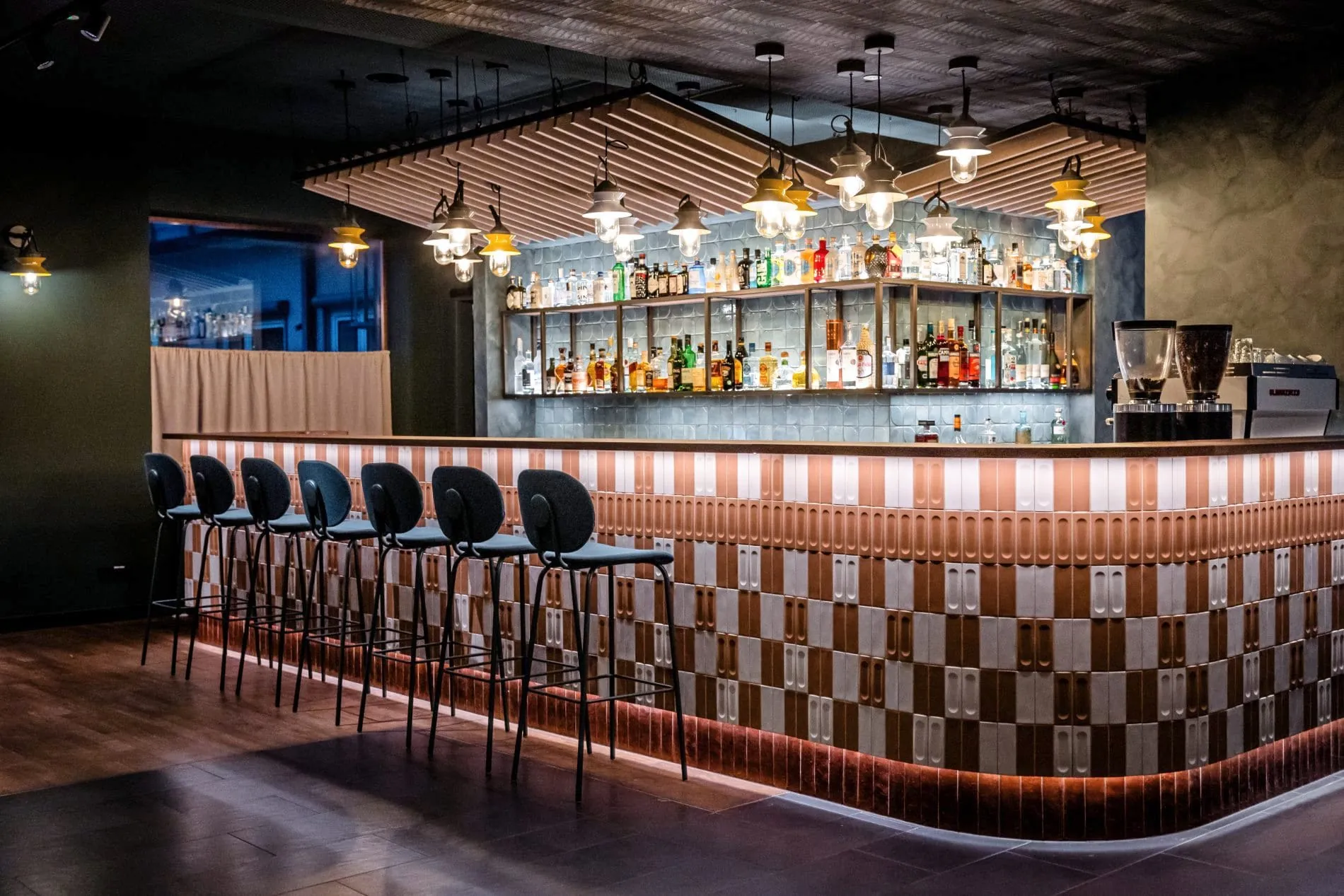 Schachbrettmuster am Tresen, hellblaue Fliesen und Hafenlampen: Die Bar bildet einen zentralen Treffpunkt im öffentlichen Bereich.